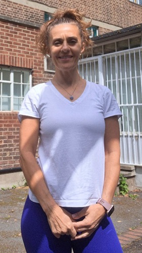Tanya standing outdoors in front of a brick building, wearing a white top and fitness watch.