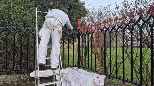 Worker repainting an old cast iron fence at St Dunstan's Church, restoring the historic railings.