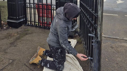 Painter restoring historic church gates at St Dunstan's, applying fresh black paint to metal railings.