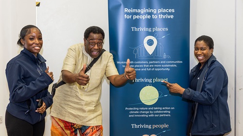 Three people standing in front of a banner about thriving places and sustainability, giving thumbs-up gestures