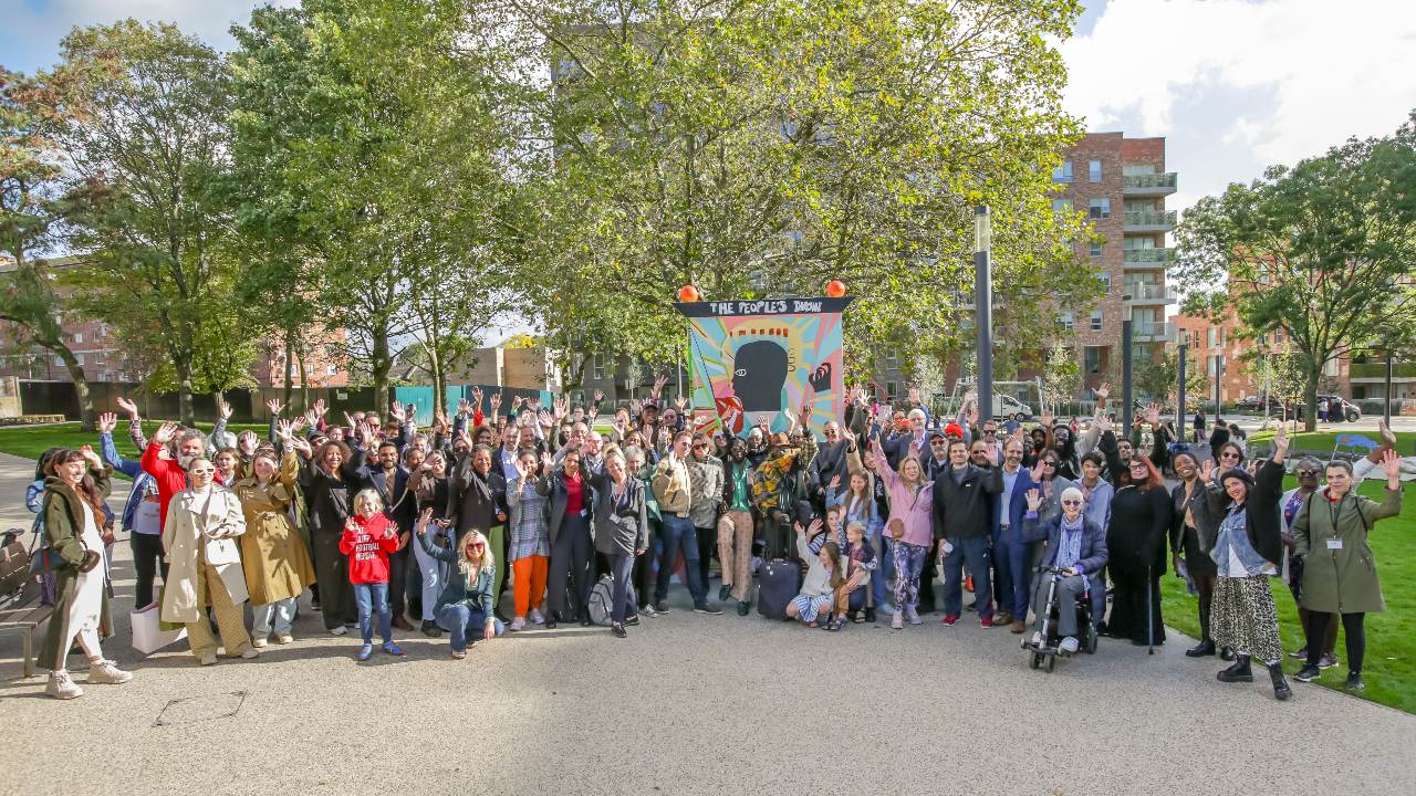 Large group of people standing in front of trees smiling and waving
