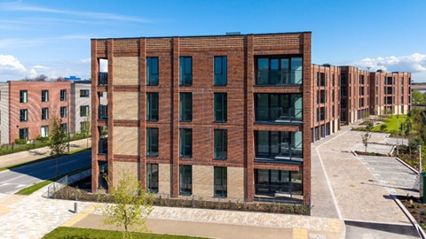 Exterior view of a modern multi-storey brick apartment building with large windows and landscaped surroundings.
