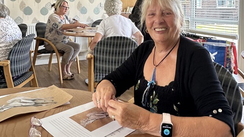 A woman smiling at the camera while working on an art piece.