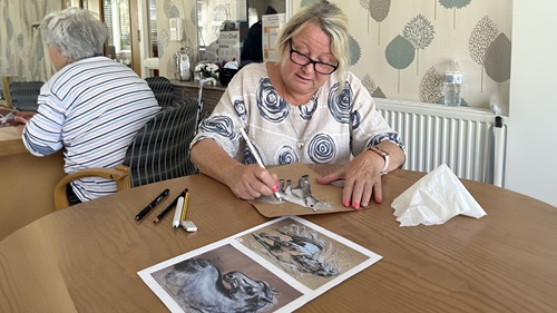 A woman concentrating on drawing a horse on brown paper.