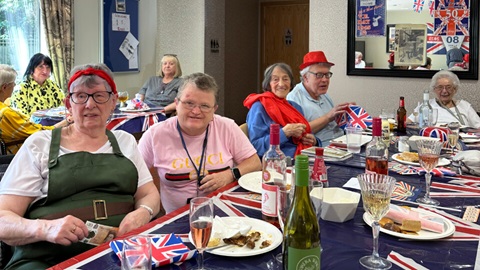 Older people celebrating VE Day with food, drinks, and Union Jack decorations