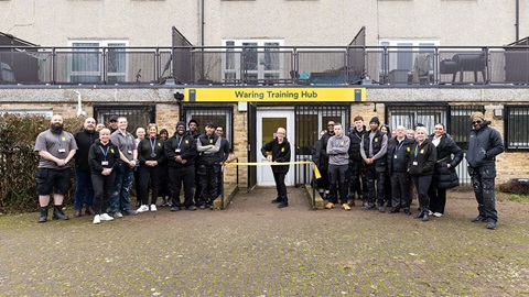 Large group of staff standing outside the Waring Training Hub building, posing together in front of the entrance.