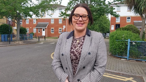 Sinead standing outdoors on a residential street, wearing glasses and a patterned top, with houses and trees behind.