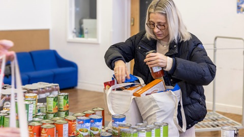 Woman packing groceries into a reusable bag from a table of donated food items