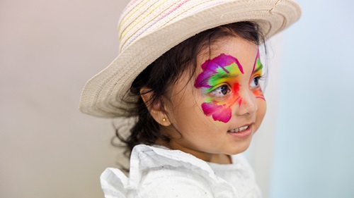 A young child with vibrant face pain on and a summer hat.