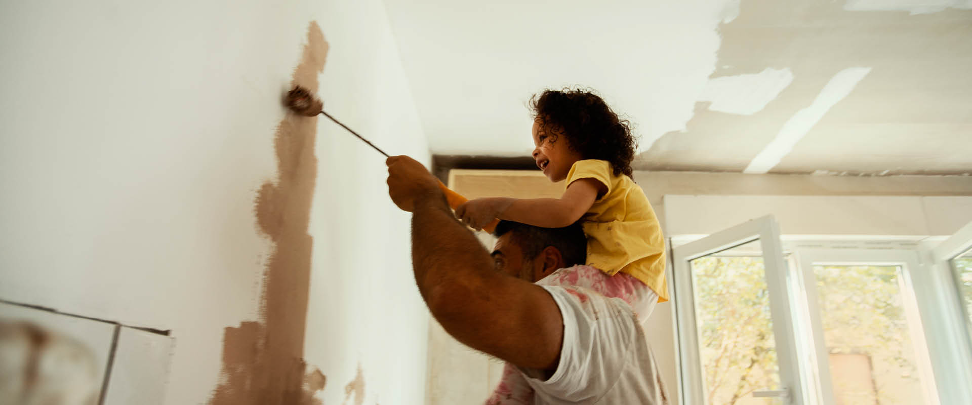 Child on father's shoulders painting internal wall