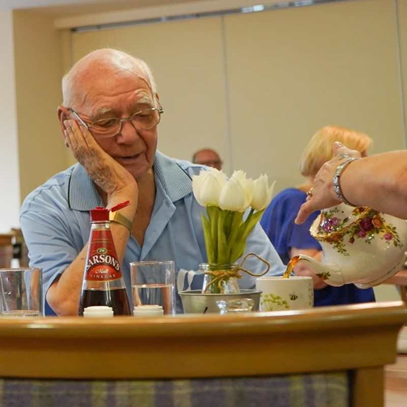 An elderly man being poured a cup of tea