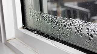 Condensation builds up on a windowpane, forming water droplets along the edge